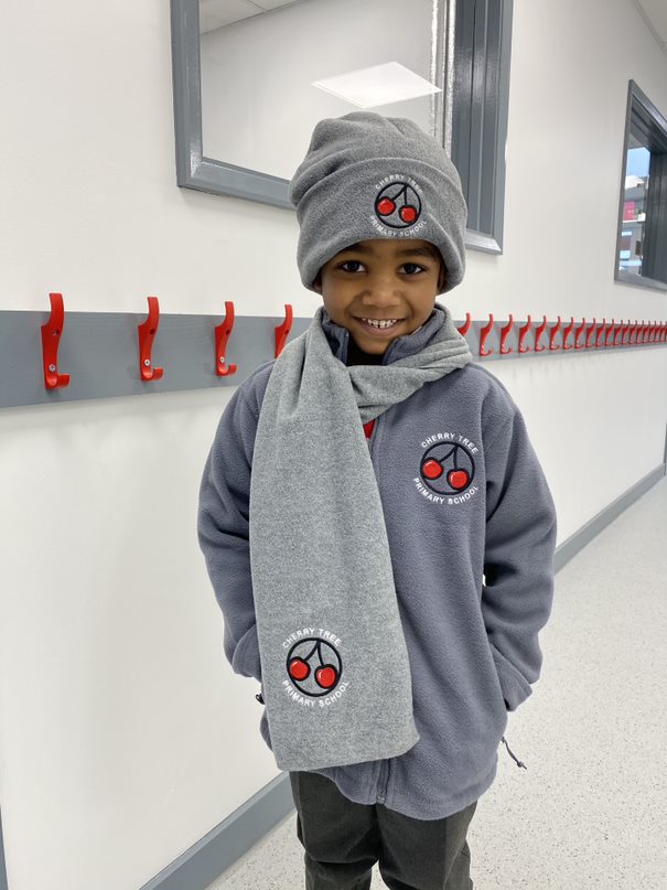 student stands in corridor wearing grey school fleece, scarf and hat
