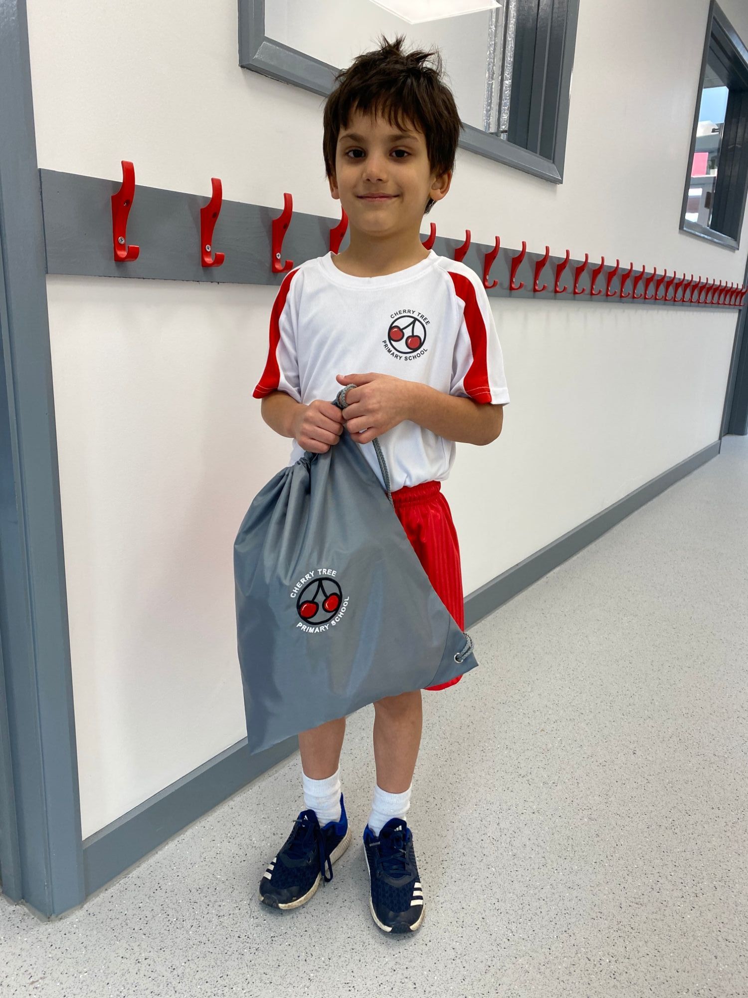 student stands in corridor PE kit and holding grey PE bag
