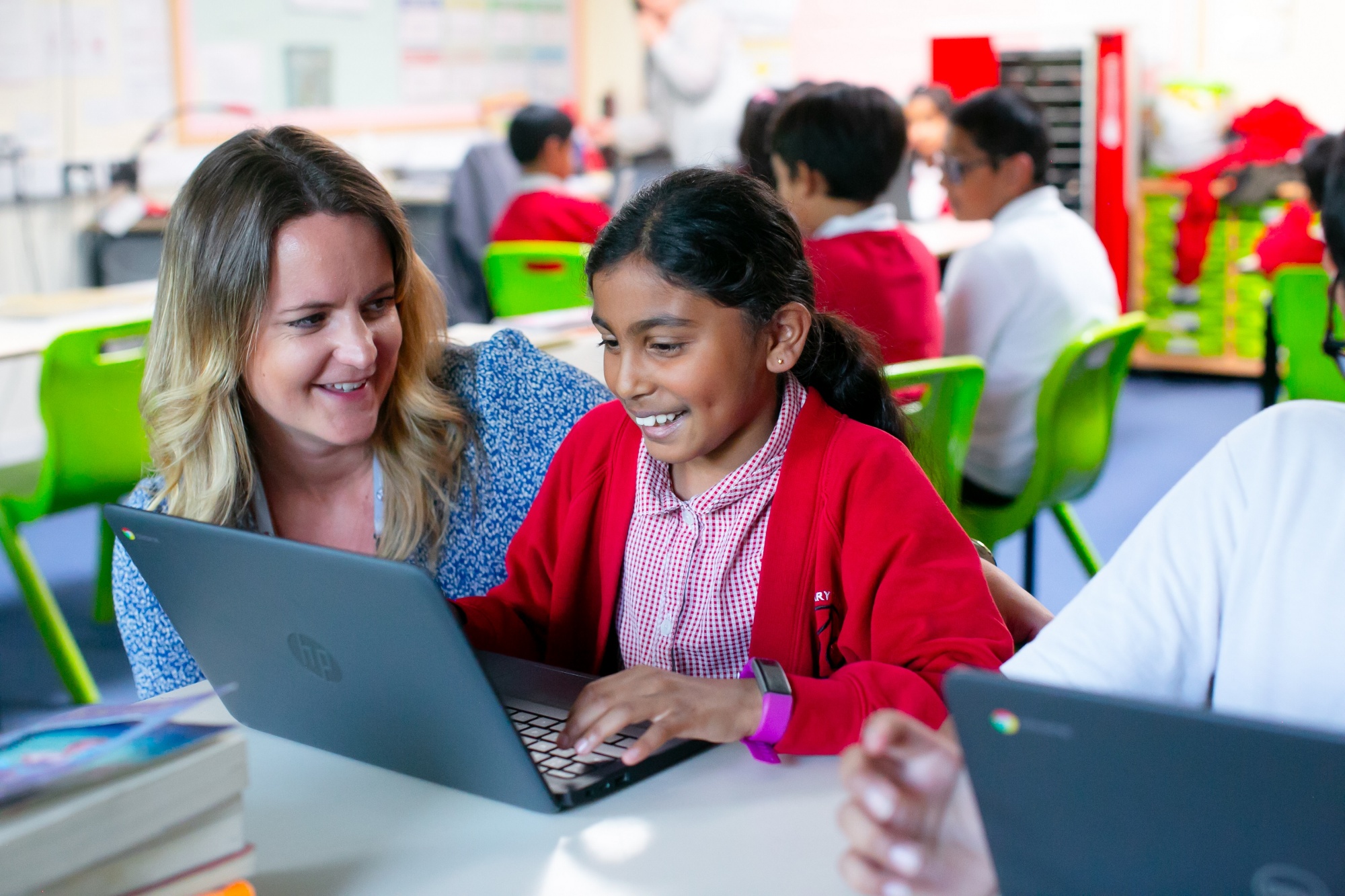 the head teacher sits with a child working on a laptop in the classroom